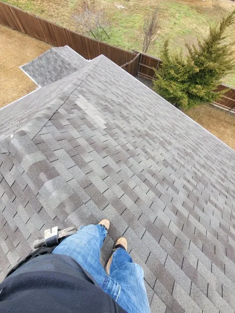 View down a gray shingle roof with a worker in the foreground